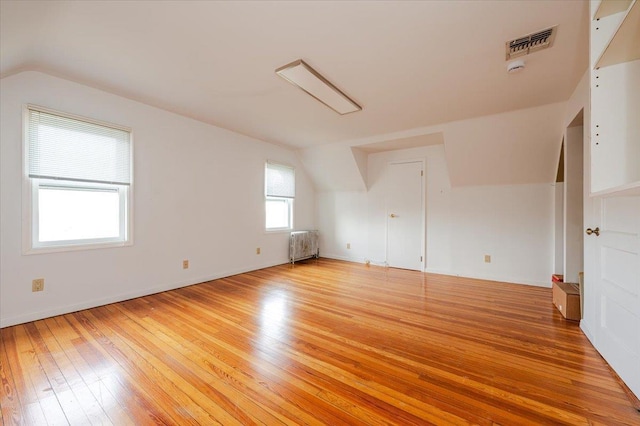 additional living space featuring lofted ceiling, light wood-style floors, radiator, and visible vents