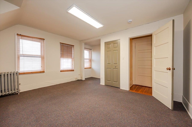 additional living space featuring a healthy amount of sunlight, radiator heating unit, dark carpet, and vaulted ceiling