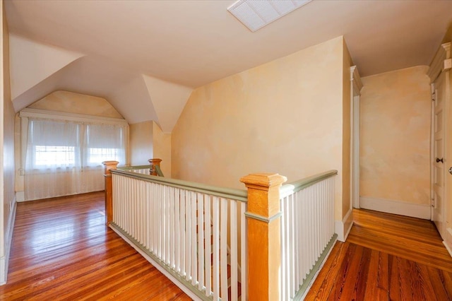 hall with vaulted ceiling, visible vents, wood finished floors, and an upstairs landing