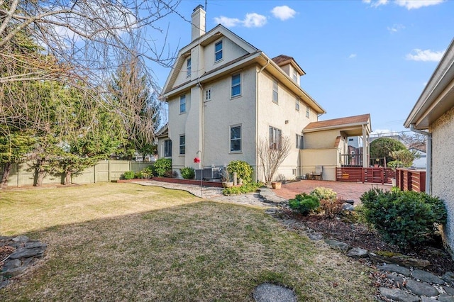 rear view of property featuring a patio, a chimney, fence, a yard, and stucco siding