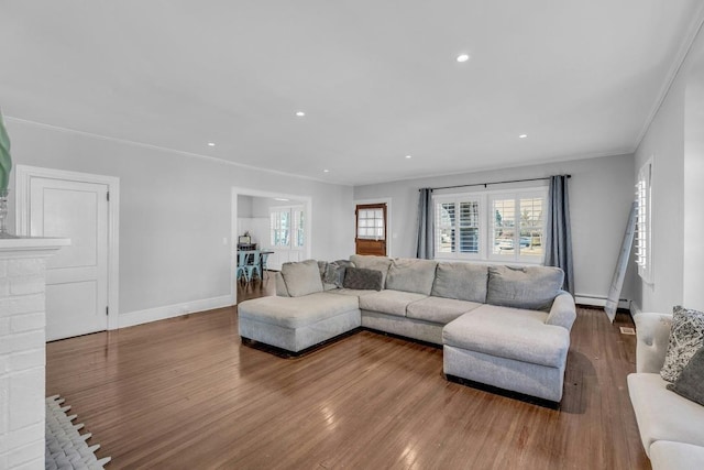 living room with recessed lighting, a baseboard heating unit, wood finished floors, baseboards, and crown molding