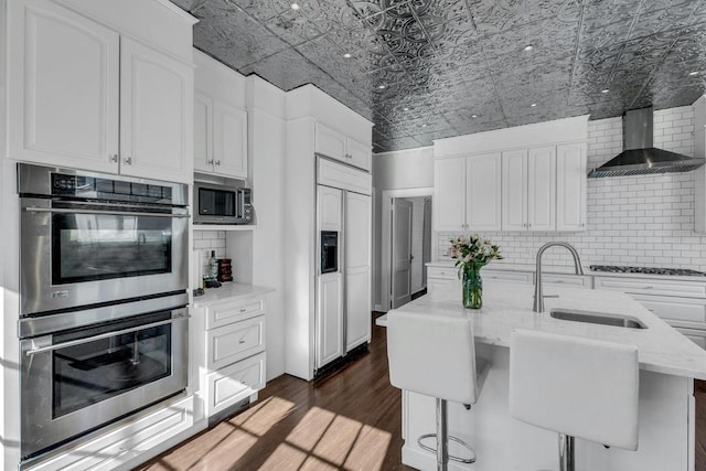 kitchen featuring an ornate ceiling, tasteful backsplash, a sink, wall chimney range hood, and built in appliances