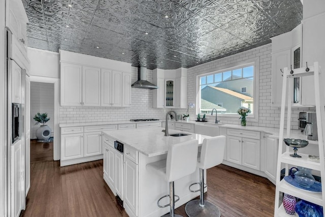 kitchen featuring dark wood-style flooring, a sink, decorative backsplash, wall chimney exhaust hood, and an ornate ceiling