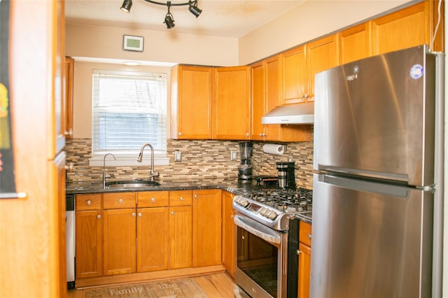 kitchen featuring under cabinet range hood, stainless steel appliances, a sink, dark stone counters, and tasteful backsplash