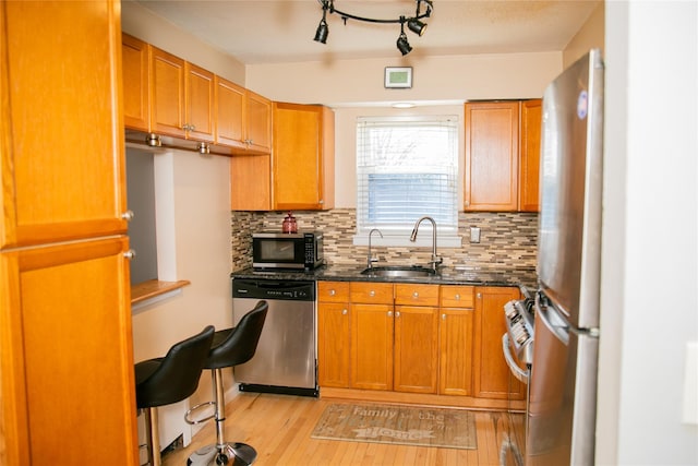 kitchen with decorative backsplash, light wood-style flooring, appliances with stainless steel finishes, brown cabinets, and a sink