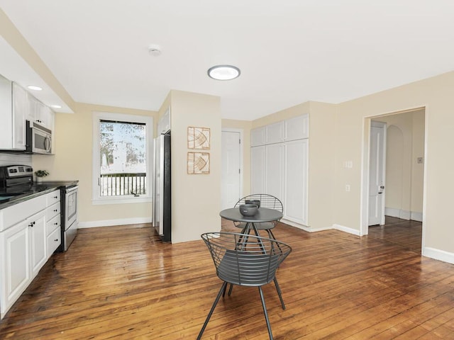 kitchen featuring stainless steel appliances, dark wood-style flooring, baseboards, white cabinets, and dark countertops