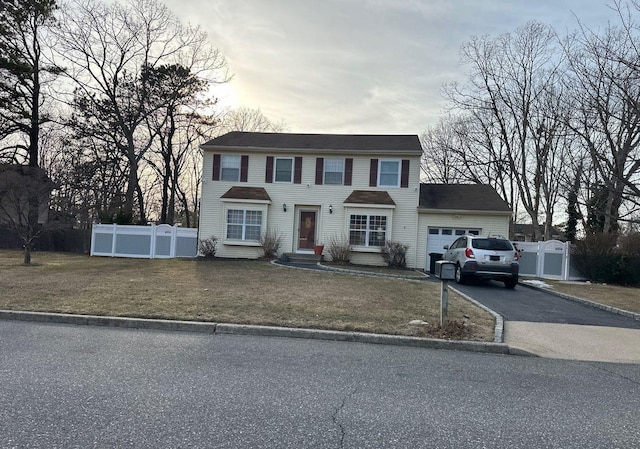 colonial house with a garage, aphalt driveway, a front yard, and fence