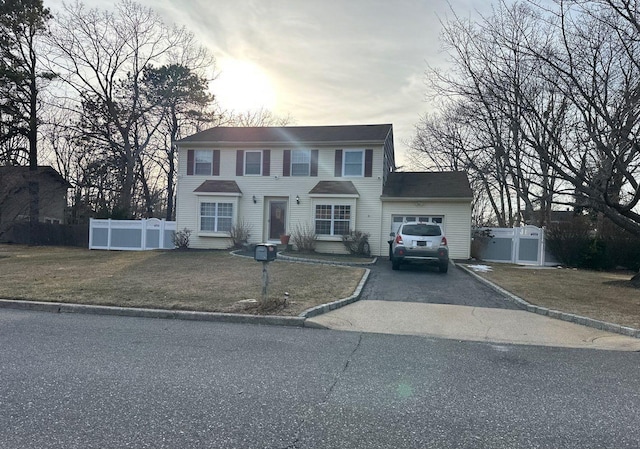 colonial-style house featuring aphalt driveway, an attached garage, fence, and a front yard