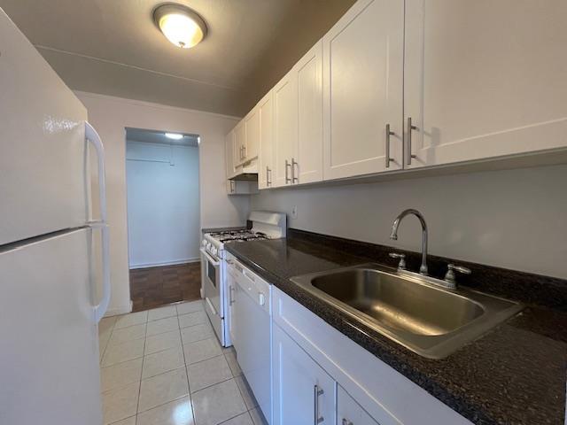 kitchen featuring white appliances, light tile patterned floors, under cabinet range hood, white cabinetry, and a sink