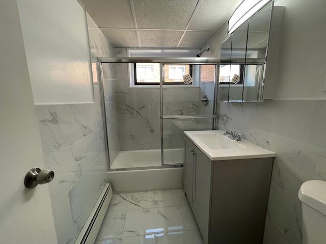 bathroom with toilet, a baseboard heating unit, vanity, tile walls, and marble finish floor