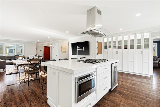 kitchen featuring built in microwave, open floor plan, island exhaust hood, stainless steel gas stovetop, and white cabinets