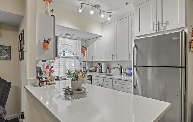 kitchen with light stone counters, a sink, freestanding refrigerator, and white cabinetry