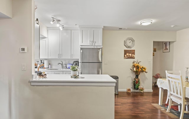 kitchen with dark wood-type flooring, freestanding refrigerator, a peninsula, light countertops, and a sink