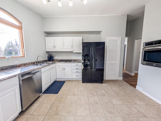 kitchen featuring appliances with stainless steel finishes, a sink, white cabinetry, and baseboards