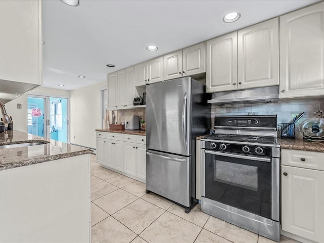 kitchen featuring under cabinet range hood, backsplash, a sink, freestanding refrigerator, and gas range
