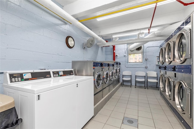 shared laundry area with concrete block wall, washer and clothes dryer, and light tile patterned flooring