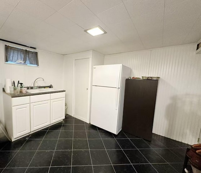 kitchen with dark tile patterned flooring, a sink, white cabinetry, freestanding refrigerator, and dark countertops