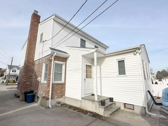 back of house with crawl space, a chimney, and brick siding