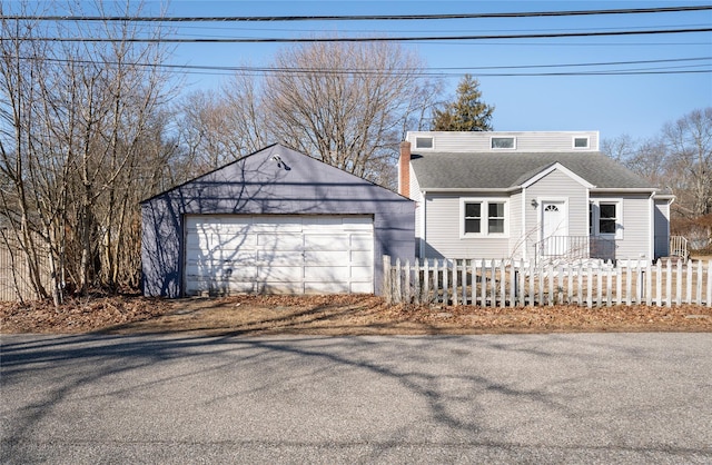 view of front of house with a fenced front yard, a detached garage, roof with shingles, and an outbuilding