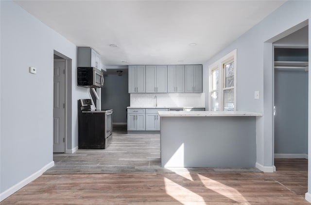 kitchen with appliances with stainless steel finishes, wood finished floors, a peninsula, light countertops, and backsplash