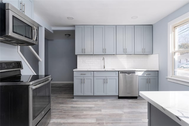 kitchen featuring tasteful backsplash, stainless steel appliances, a sink, and gray cabinetry