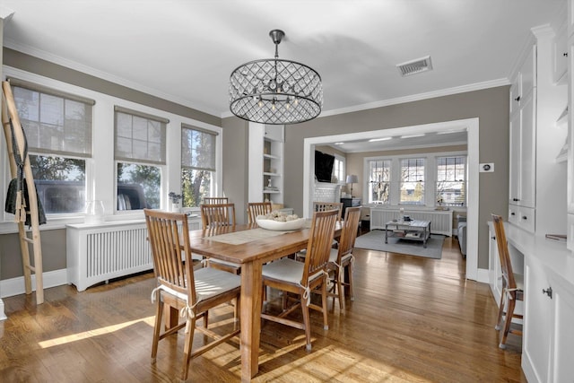 dining room featuring wood finished floors, visible vents, baseboards, ornamental molding, and a brick fireplace