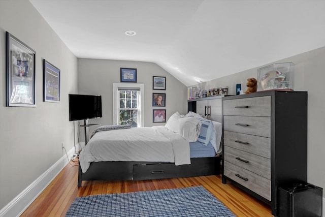 bedroom with vaulted ceiling, wood finished floors, and baseboards