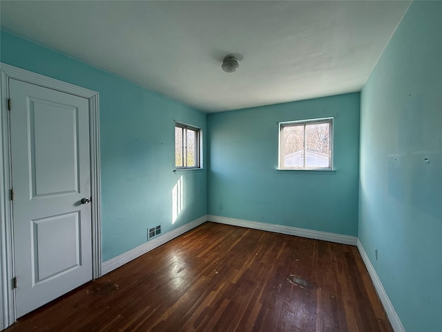 unfurnished room featuring dark wood finished floors, visible vents, and a healthy amount of sunlight