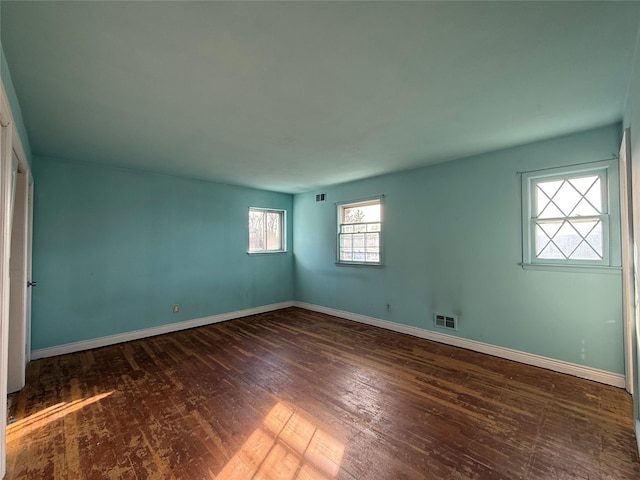 unfurnished room featuring baseboards, visible vents, and dark wood finished floors