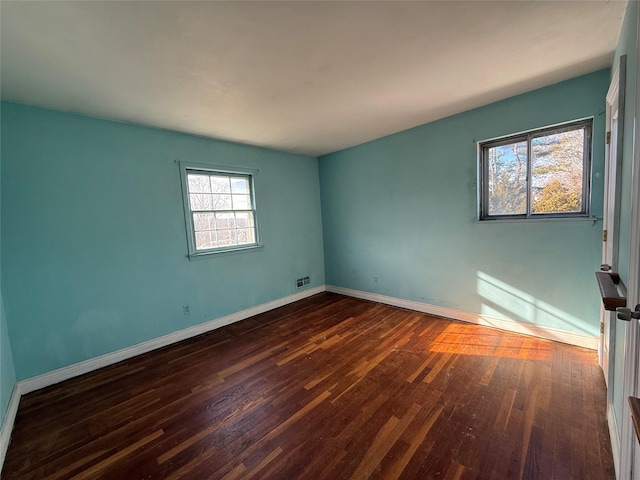 spare room featuring dark wood-style floors, visible vents, and baseboards