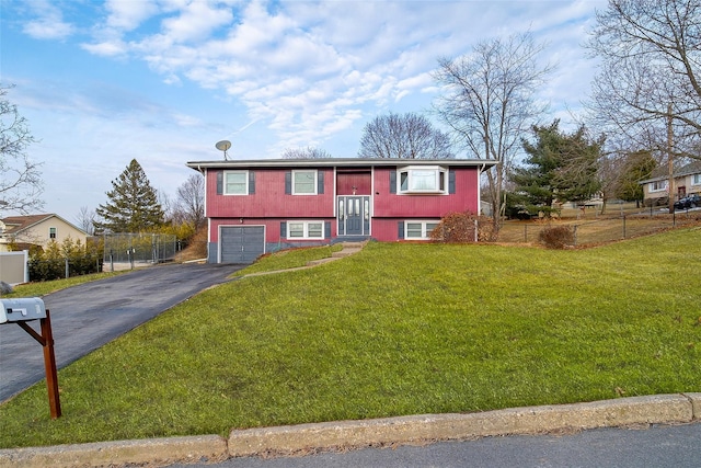 raised ranch featuring aphalt driveway, an attached garage, fence, and a front yard