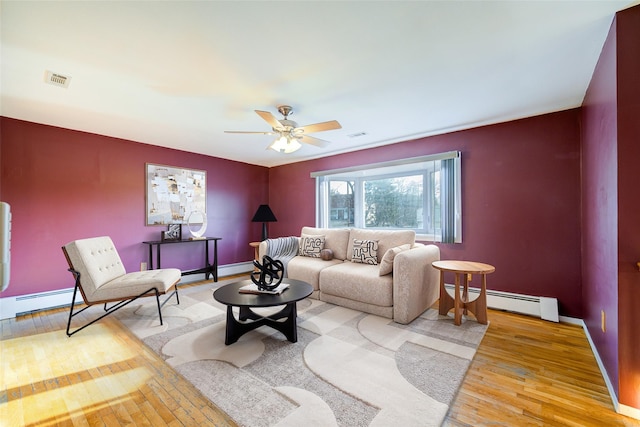 living area with light wood finished floors, baseboard heating, baseboards, and a ceiling fan