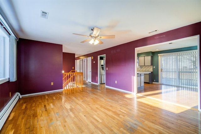 spare room with baseboards, visible vents, light wood-type flooring, and a baseboard radiator