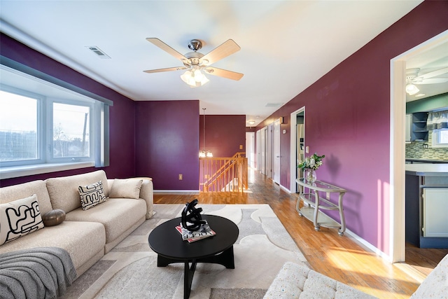 living area with a ceiling fan, wood finished floors, visible vents, and baseboards