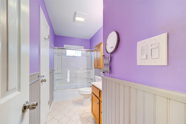 full bath with vanity, a wainscoted wall, shower / bath combination with glass door, tile patterned flooring, and toilet