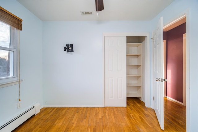 unfurnished bedroom featuring light wood-style floors, visible vents, baseboard heating, and baseboards