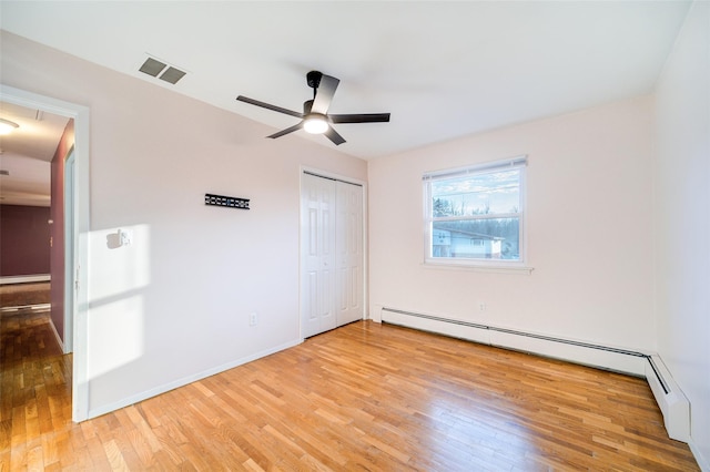 unfurnished bedroom featuring visible vents, a baseboard heating unit, a closet, light wood-style floors, and baseboards