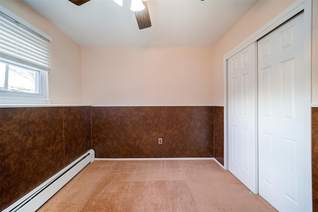 unfurnished bedroom with a closet, carpet floors, wainscoting, baseboard heating, and ceiling fan