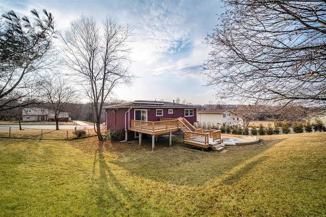 rear view of property with a yard, solar panels, a deck, and fence