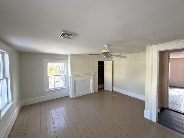 unfurnished room featuring a ceiling fan, wood finished floors, visible vents, and baseboards