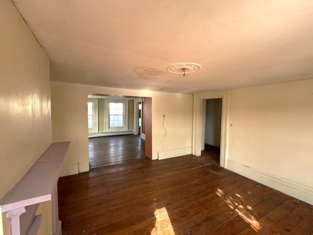 spare room featuring baseboards, baseboard heating, and dark wood-type flooring