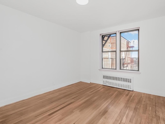 spare room with radiator heating unit, baseboards, and wood finished floors