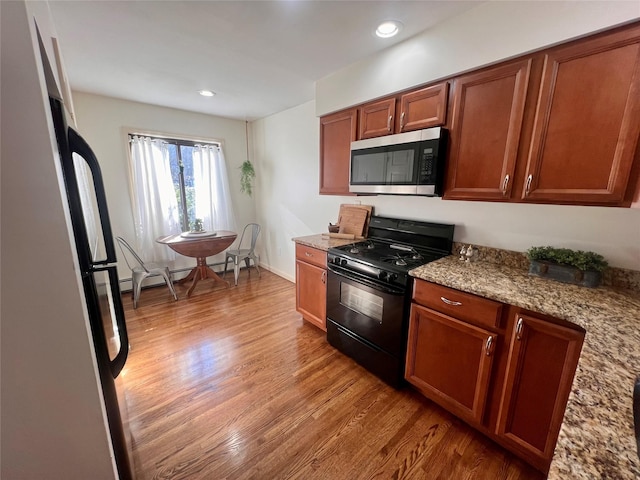 kitchen featuring light stone countertops, wood finished floors, brown cabinets, stainless steel microwave, and black gas range oven