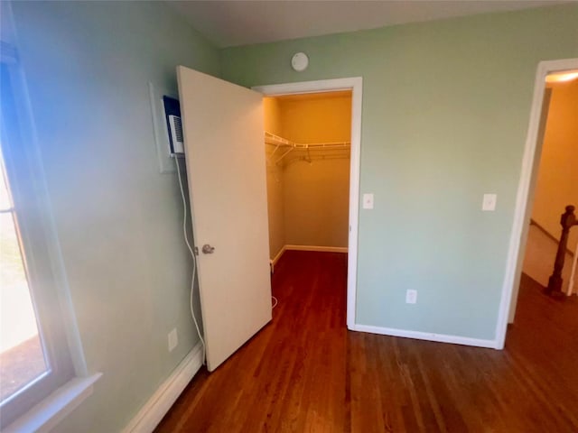 unfurnished bedroom with baseboards, a walk in closet, and wood finished floors