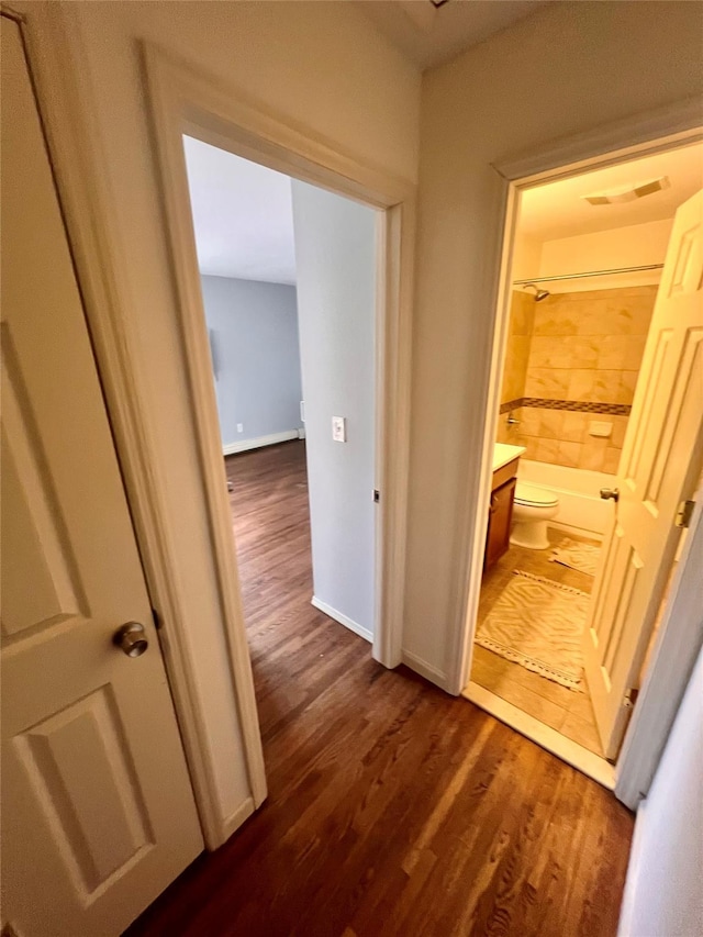 hallway featuring dark wood-type flooring, visible vents, and baseboards