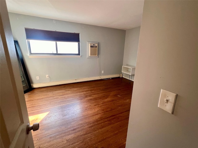 spare room featuring baseboards, a baseboard heating unit, wood finished floors, and a wall mounted air conditioner