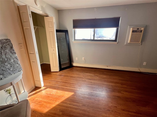 unfurnished bedroom with a baseboard radiator, baseboards, an AC wall unit, and wood finished floors