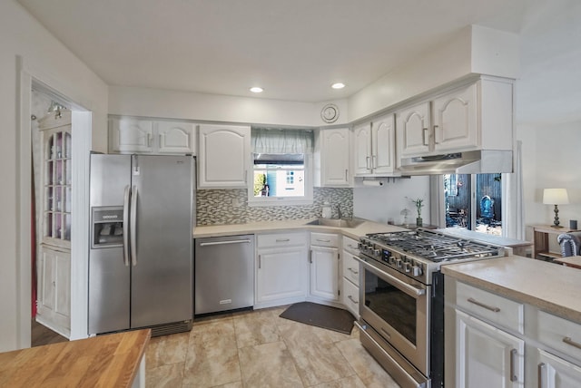 kitchen with tasteful backsplash, white cabinets, stainless steel appliances, light countertops, and under cabinet range hood