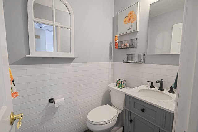 half bathroom featuring toilet, a wainscoted wall, tile walls, and vanity