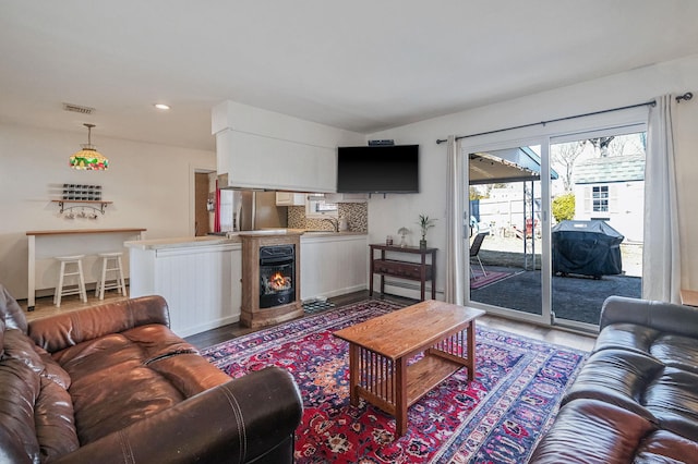 living room featuring recessed lighting, beverage cooler, wood finished floors, visible vents, and a lit fireplace